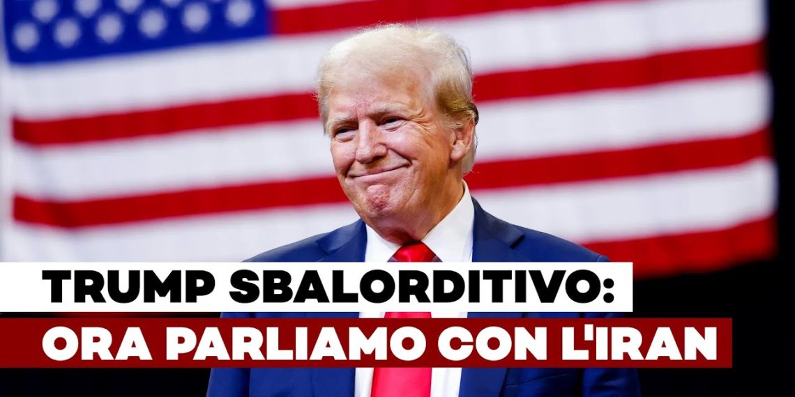 Donald Trump sorride con la bandiera degli USA alle spalle